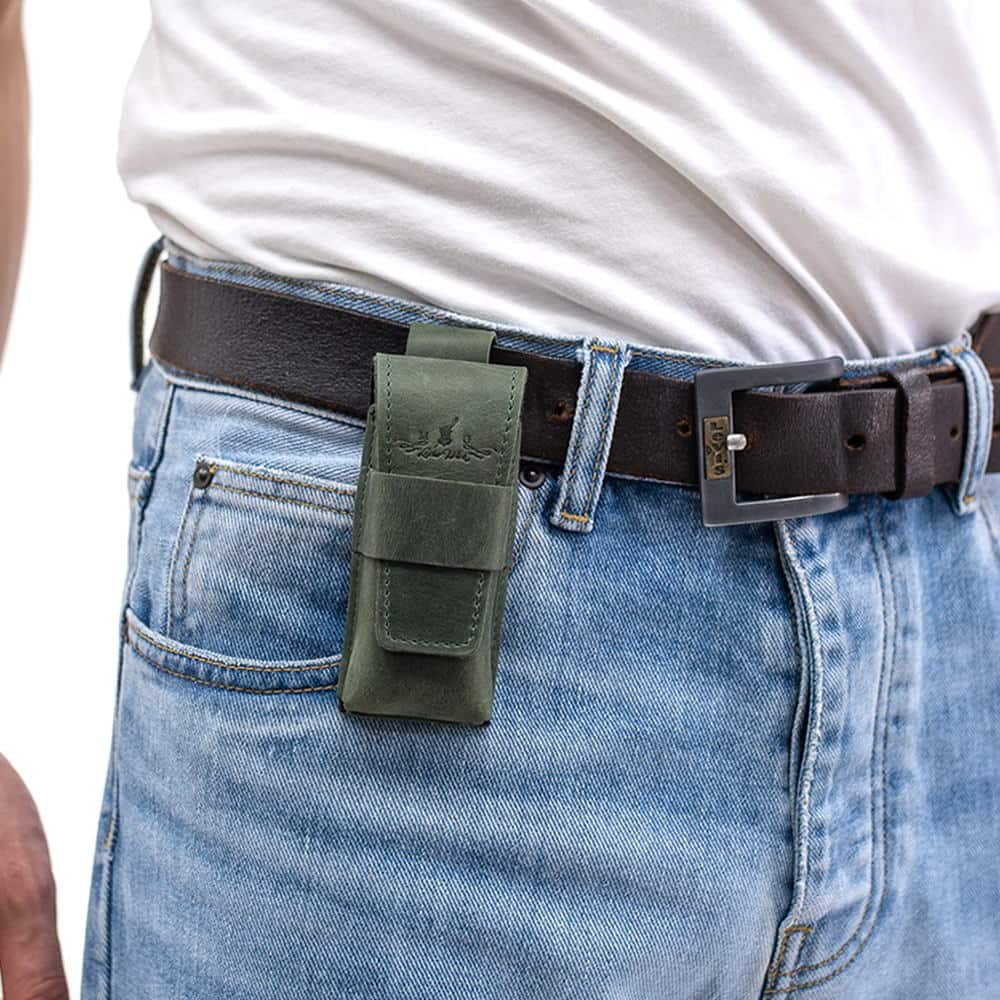 Green leather harmonica case attached to black belt on jeans.