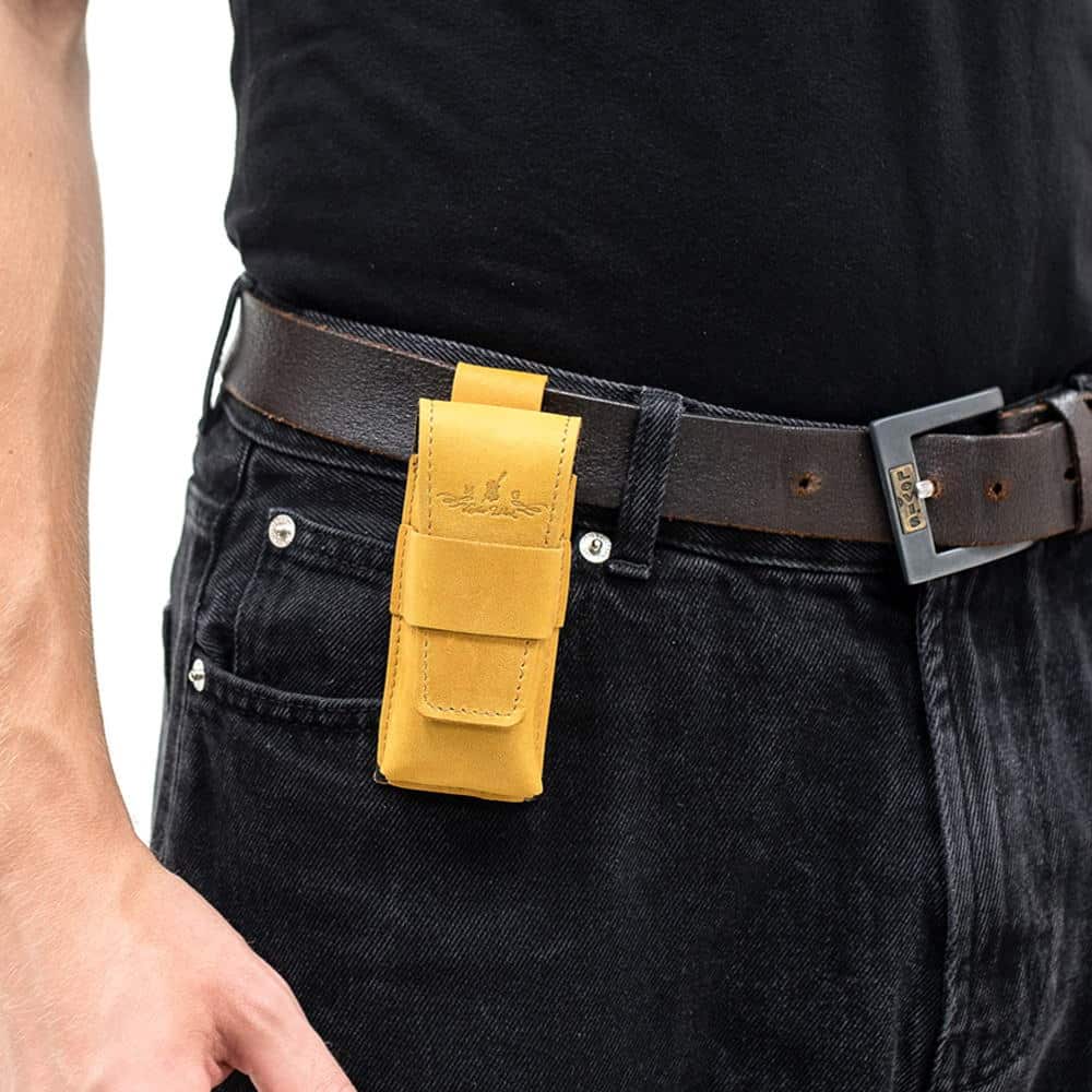 Yellow leather harmonica case mounted on black belt over jeans.